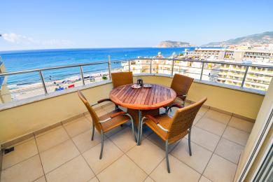 Alanya woning balkon met een houten tafel, rieten stoelen en prachtig uitzicht op zee onder helder zonlicht.