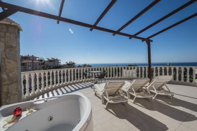 Sunčani balkon nekretnine u Alanji sadrži jacuzzi, ležaljke i zadivljujući pogled na more ispod drvene pergole.