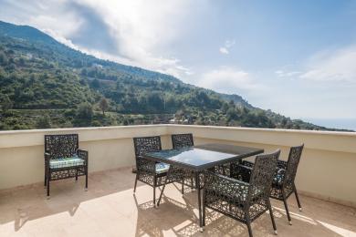 Balkon nekretnine u Alanji sa nameštajem od pruća, podom od pločica i zadivljujućim pogledom na planine pod vedrim, sunčanim nebom.