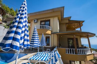 Alanya mulkining tashqi ko'rinishi, unda basseyn, yo'lli soyabonlar va dengiz manzarali balkon mavjud.