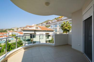 Yorqin Alanya balkonida shisha panjaralar, kafel qoplamasi va atrofdagi binolarning go'zal manzaralari mavjud.