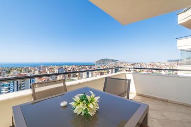 Alanya mulkidagi shahar va dengiz manzarali balkon, shisha stol va tashqi o'rindiqlarga ega.