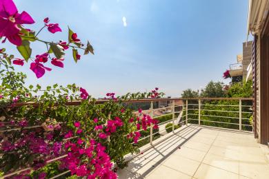 Alanyai ingatlan erkélye élénk bougainvilleával, fehér csempepadlóval és panorámás városi kilátással a napsütéses ég alatt.