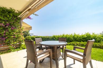 Alanya mulkidagi rattan mebellar, shisha stol va yashil o'simliklar bilan jihozlangan balkon yorqin va osoyishta muhitni taqdim etadi.