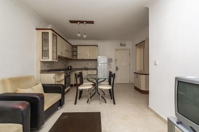 Alanja apartman dnevni boravak sadrži kuhinju, trpezarijski sto i udobno sedenje sa neutralnim tonovima i jakim osvetljenjem.