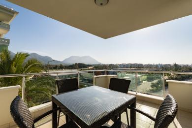 Alanya mulkidagi shisha panjarali balkon, tol mebellari va yorqin, tabiiy yorug'lik ostida ajoyib tog' manzaralari.
