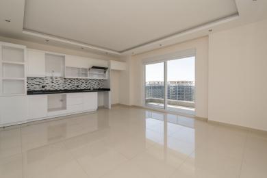 Svetli apartman u Alanji ima modernu belu kuhinju sa mozaik pozadinom i pristup balkonu, stvarajući prostran osećaj.