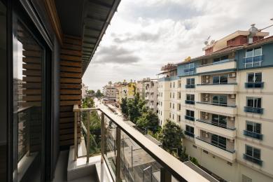 Balkon nekretnine u Alanji sa staklenim ogradama, drvenim detaljima i pogledom na grad pod oblačnim nebom.