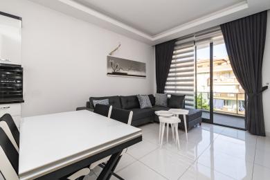 Svijetli apartman u Alanji, dnevni boravak s pristupom balkonu, s sivom sofom, bijelim stolom i podom od pločica.