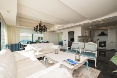 Helles Wohnzimmer in Alanya mit weißen Sofas, schwarzem Kronleuchter und offener Küche mit Marmorböden und Meerblick.