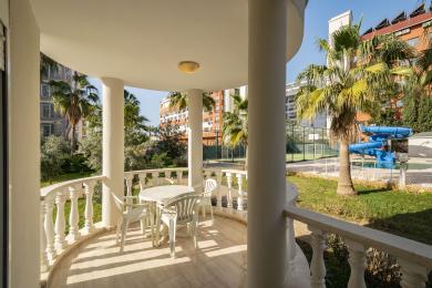Балкон в Аланье с белыми колоннами, плиточным полом и открытой площадкой с видом на пышную тропическую территорию.