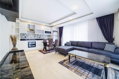 Svijetli dnevni boravak u apartmanu u Alanji s modernom kuhinjom, plišanim kaučem i elegantnim mramornim detaljima.