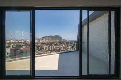 Svijetli balkon u Alanji sa staklenim ogradama nudi zadivljujući pogled na grad i more kroz velika klizna staklena vrata.