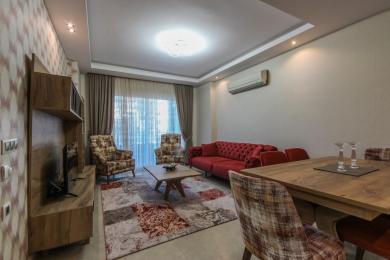 Alanya mulkidagi qizil divan, naqshli stullar va yorqin, jozibali yoritishga ega yashash xonasi.