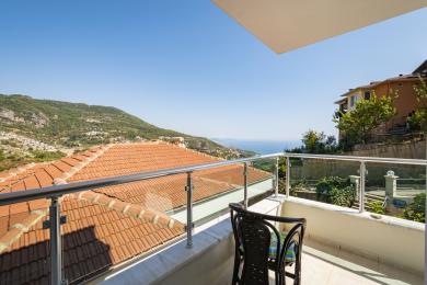 Balkon nekretnine u Alanji sa staklenom ogradom koji nudi zadivljujući pogled na planine i more pod jakom, prirodnom svetlošću.