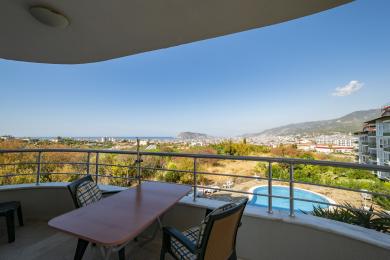 Alanya mulkidagi stol, stullar va shahar, dengiz va basseynning panoramik ko'rinishlari bilan balkon.