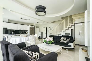Яркая гасцёўня ў Алані з адкрытай планіроўкай, сучаснай белай кухняй, лесвіцай і стыльнай чорна-белай мэбляй.