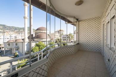 Balkon nekretnine u Alanji sa staklenim kućištem, popločanim podom i zidovima, nudi svijetao pogled na grad i džamiju.