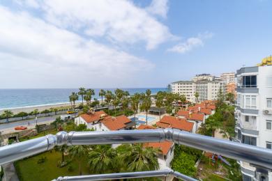 Balkonblick auf eine Immobilie in Alanya mit Blick auf das Mittelmeer, Palmen und nahegelegene Gebäude unter einem hellen, sonnigen Himmel.