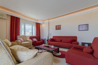 Qizil divanlar, iliq yoritgichlar va tog' manzaralari bilan o'ralgan Alanya yashash xonasi.