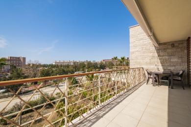 Alanya mulkidagi tosh devorli, kafel pollari, metall panjarasi va yorqin quyosh nurlari ostida shahar manzarasi bo'lgan balkon.