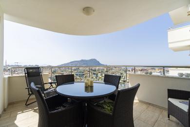 Balkon nekretnine u Alanji sa nameštajem od pruća i zadivljujućim pogledom na grad i planine pri jakoj dnevnoj svetlosti.