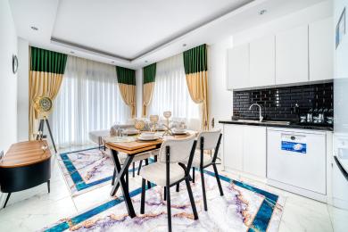 Alanya eiendom: Lyst, moderne spiseområde med hvite skap, svart bakplate og stilige gull- og grønne gardiner.