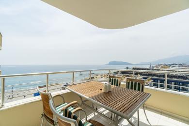 Alanya mülkündə taxta masa, stullar və parlaq, təbii işıq altında gözəl dəniz mənzərələri olan balkon.