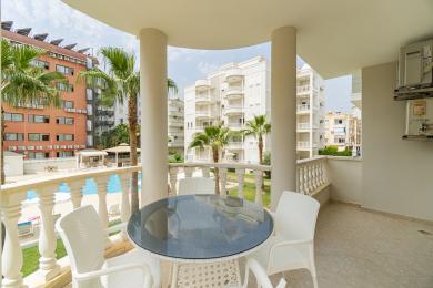 Oq ustunlar, shisha usti stol va basseyn va palma daraxtlari manzarasi bilan Alanya mulkidagi balkon.