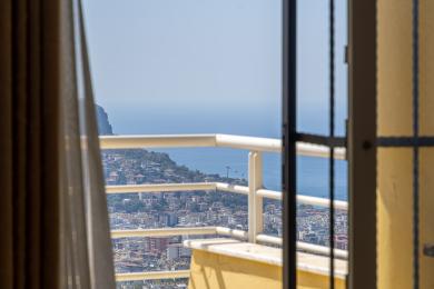 Balkon nekretnine u Alanji s prekrasnim pogledom na more i grad kroz svijetla, suncem okupana staklena vrata i bijele ograde.