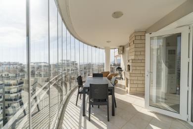 Svetli, zatvoreni balkon u Alanji sadrži trpezarijski set, kameni kamin i panoramski pogled na grad.