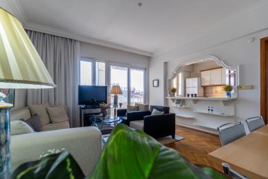 اتاق نشیمن ملک آلانیا دارای کفپوش پارکت، صندلی های راحت و آشپزخانه اوپن با نور طبیعی روشن.