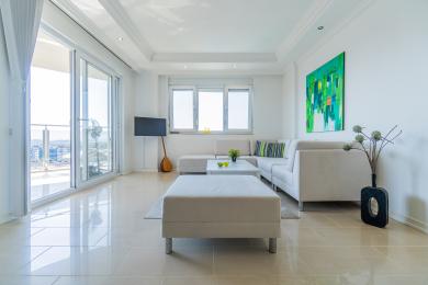 Lichte Alanya woonkamer met tegelvloeren, witte sectionale bank en grote ramen die uitzicht bieden op de stad.