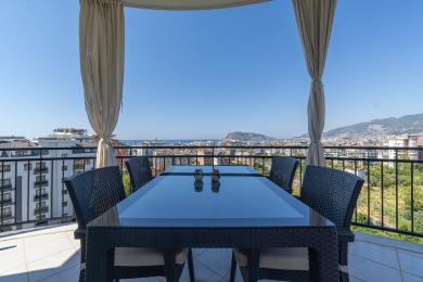 Alanya-Immobilienbalkon mit Korbmöbeln, Glastisch und atemberaubendem Blick auf die Stadt und das Meer.