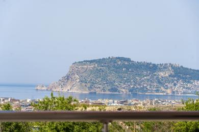 Alanya mulkidagi balkonning yorqin kunduzgi yorug'lik ostida shahar, dengiz va Alanya qal'asini namoyish etuvchi manzarasi.