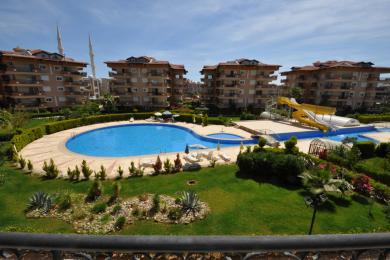 Alanya mulkining katta basseyn, suv slaydlari, yam-yashil bog'lar va yorqin osmon ostidagi ko'p qavatli uylarni namoyish etadi.