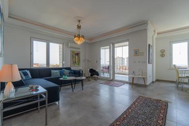 Jasny salon w apartamencie z dostępem do balkonu, prezentujący widoki na miasto i eleganckie oświetlenie żyrandolowe.