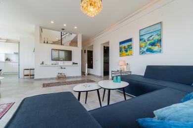 Lyst, moderne villa interiør, der viser et åbent opholdsområde med stilfulde møbler og et glimt af køkkenet og trappen.