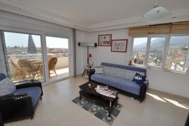 Svijetli apartman u Alanji, dnevni boravak s pristupom balkonu, podovi od pločica i pogled na grad s velikih prozora.