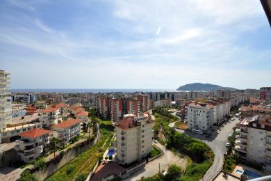 Alanya uitzicht: Een helder, zonnig stadsbeeld met de Middellandse Zee en bergen in de verte.