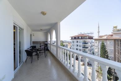 Oq balustrad, kafel pol va shahar manzaralariga ega Alanya mulkidagi balkon, yorug', havodor muhit yaratadi.