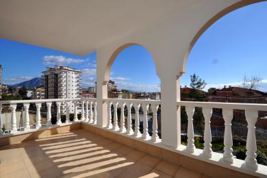 Svetli balkon u Alanji sa lučnim otvorima, belom balustradom i podom od pločica koji nudi pogled na grad.
