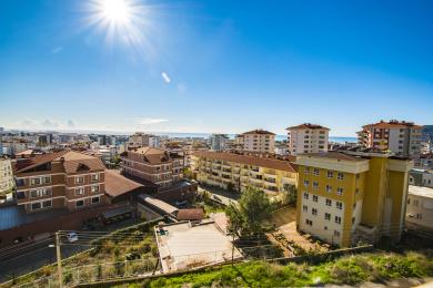 Alanya ingatlan kilátás, amely bemutatja a város látképét, a Földközi-tengert és a ragyogó napsütést.