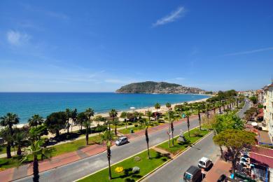 Pogled s balkona nekretnine u Alanji koji prikazuje plažu, palme i vedro plavo nebo na sunčan dan.