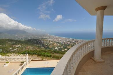 Alanya woning met balkon met stenen balustrade, zwembad en panoramisch uitzicht op de kust onder een heldere hemel.