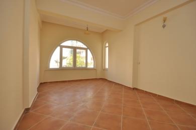 Yorugʻ, boʻsh Alanya xonasi terracotta plitka pol, kemerli deraza va iliq, neytral rangdagi devorlar bilan.