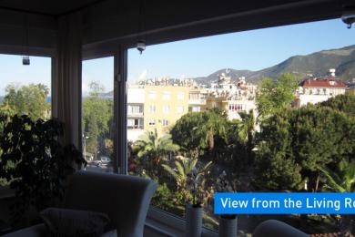 Alanya mulkidagi mehmonxonaning ko'rinishi serhosil ko'katlar va uzoqdagi tog'larni yorqin, keng derazalar orqali namoyish etadi.