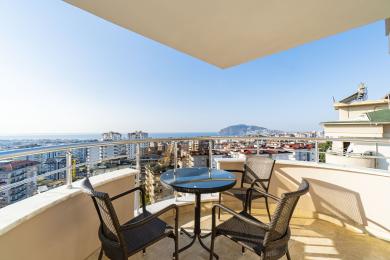 Balkon nekretnine u Alanji sa stolicama od pruća, staklenim stolom i panoramskim pogledom na grad i more.