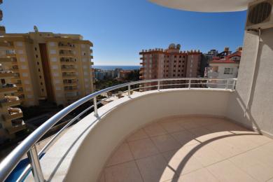 Balcon în proprietate Alanya cu podele din gresie, balustradă din oțel inoxidabil și soare strălucitor cu vedere la oraș și mare.
